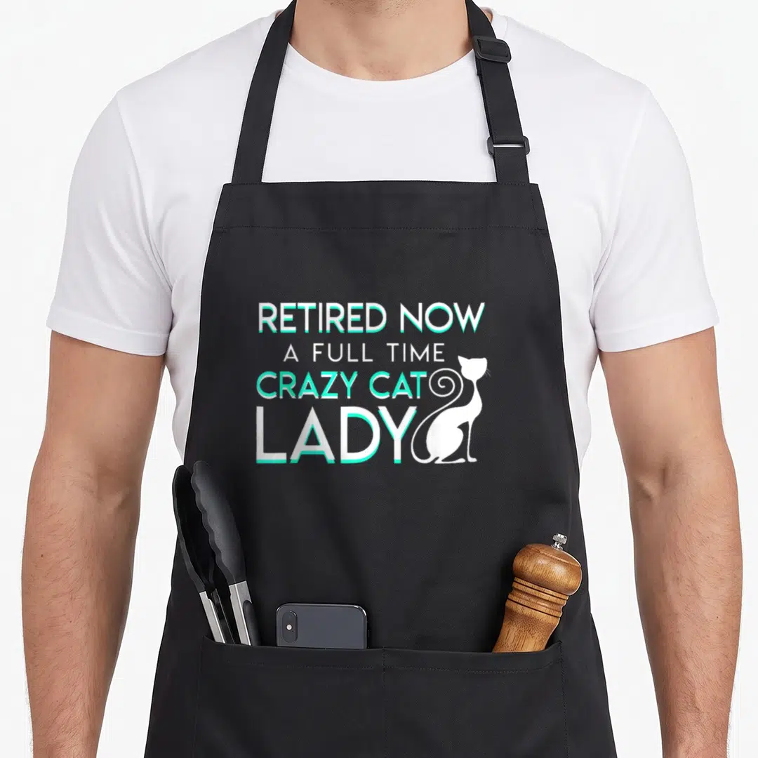 Retired crazy cat lady apron - Stacked white text reading Retired Now A Full Time Crazy Cat Lady with cat silhouette — shown on a black cotton canvas apron against a white background