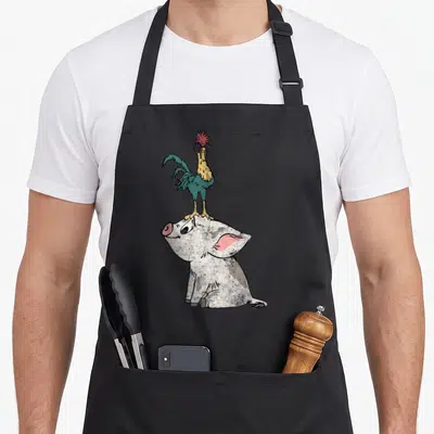 Standing novelty apron - Cartoon white pig sitting with teal rooster standing on head — shown on a black cotton canvas apron against a white background