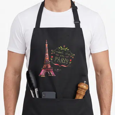 Meet paris apron - Watercolor Eiffel Tower in pink and red next to a floral wreath with text meet me in Paris — shown on a black cotton canvas apron against a white background
