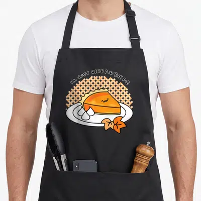 Gudetama pie apron - I'M JUST HERE FOR THE PIE text over orange pie slice with bow on checkered background — shown on a black cotton canvas apron against a white background