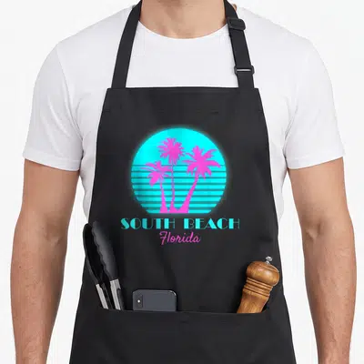 South beach florida apron - Cyan sun with horizontal stripes and three magenta palm trees above SOUTH BEACH Florida text — shown on a black cotton canvas apron against a white background