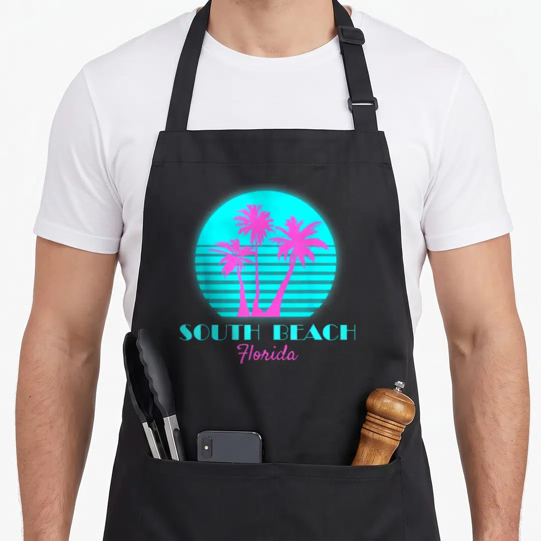 South beach florida apron - Cyan sun with horizontal stripes and three magenta palm trees above SOUTH BEACH Florida text — shown on a black cotton canvas apron against a white background