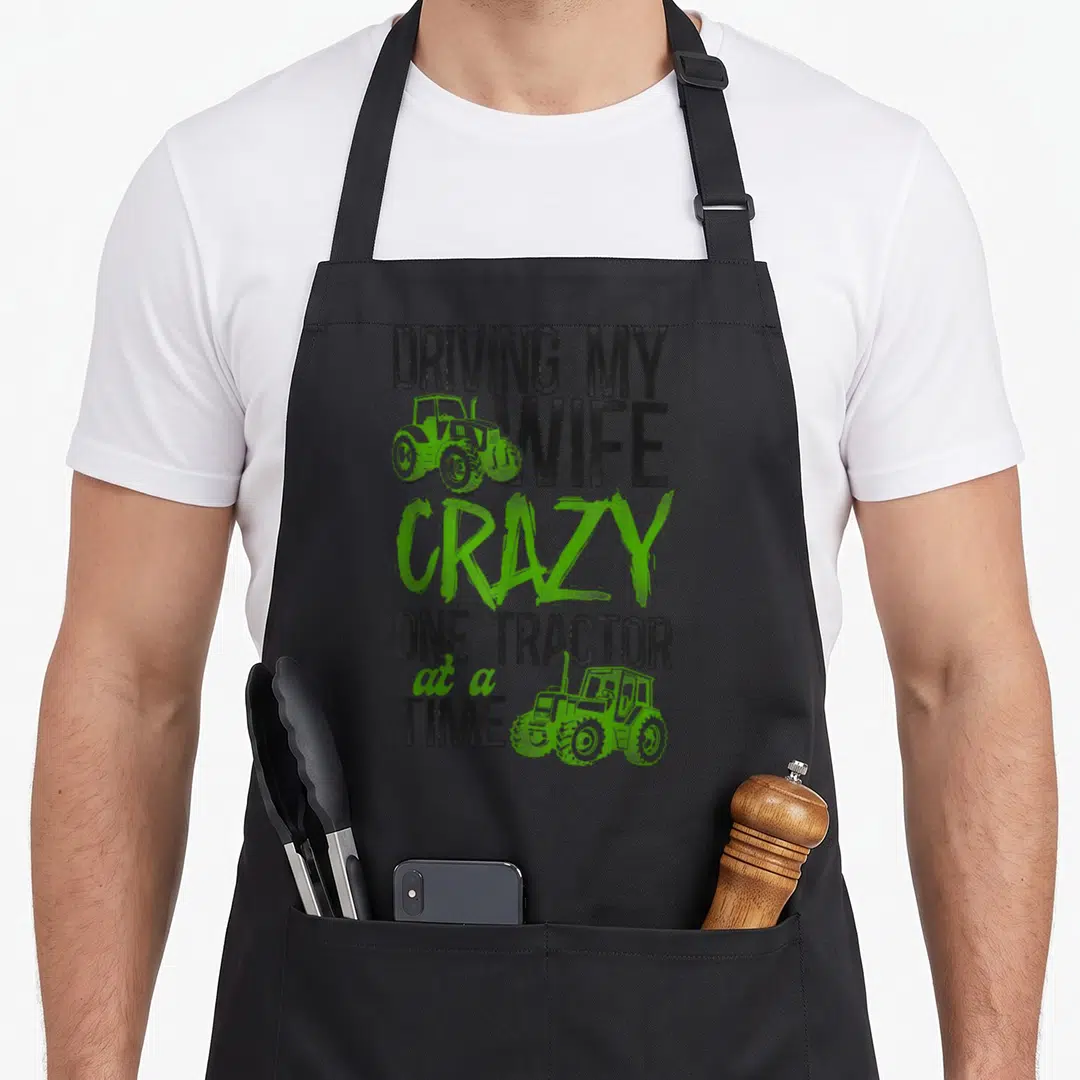 Farming driving aprons - Stacked text Dr My Wife Crazy One Tractor at a Time with two lime green tractor graphics — shown on a black cotton canvas apron against a white background