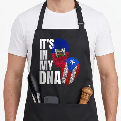 Haitian puerto heritage aprons - IT'S IN MY DNA text beside two fingerprints filled with Haitian and Puerto Rican flags — shown on a black cotton canvas apron against a white background