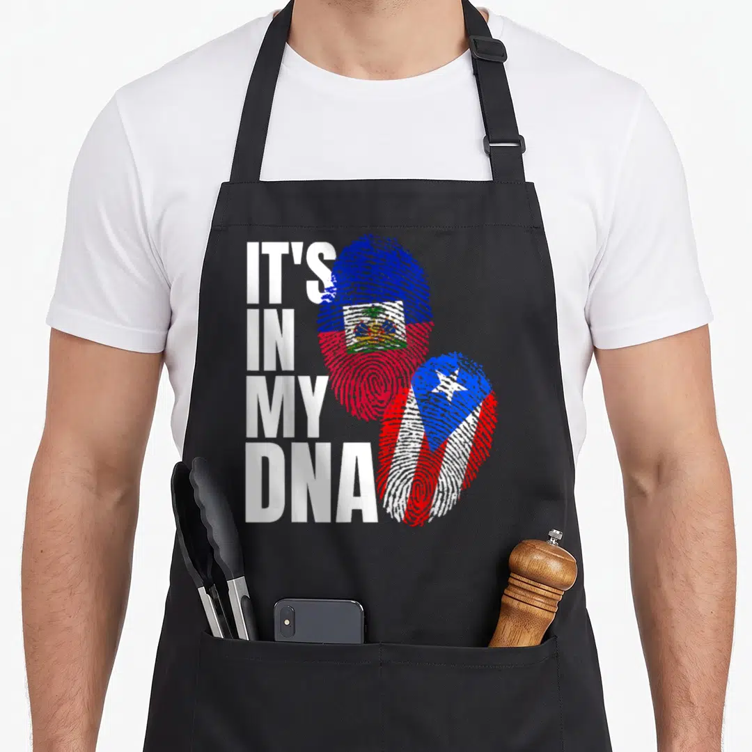 Haitian puerto heritage aprons - IT'S IN MY DNA text beside two fingerprints filled with Haitian and Puerto Rican flags — shown on a black cotton canvas apron against a white background