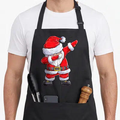 Christmas santa claus apron - Cartoon Santa Claus in red suit performing a dab dance pose with white beard and black — shown on a black cotton canvas apron against a white background
