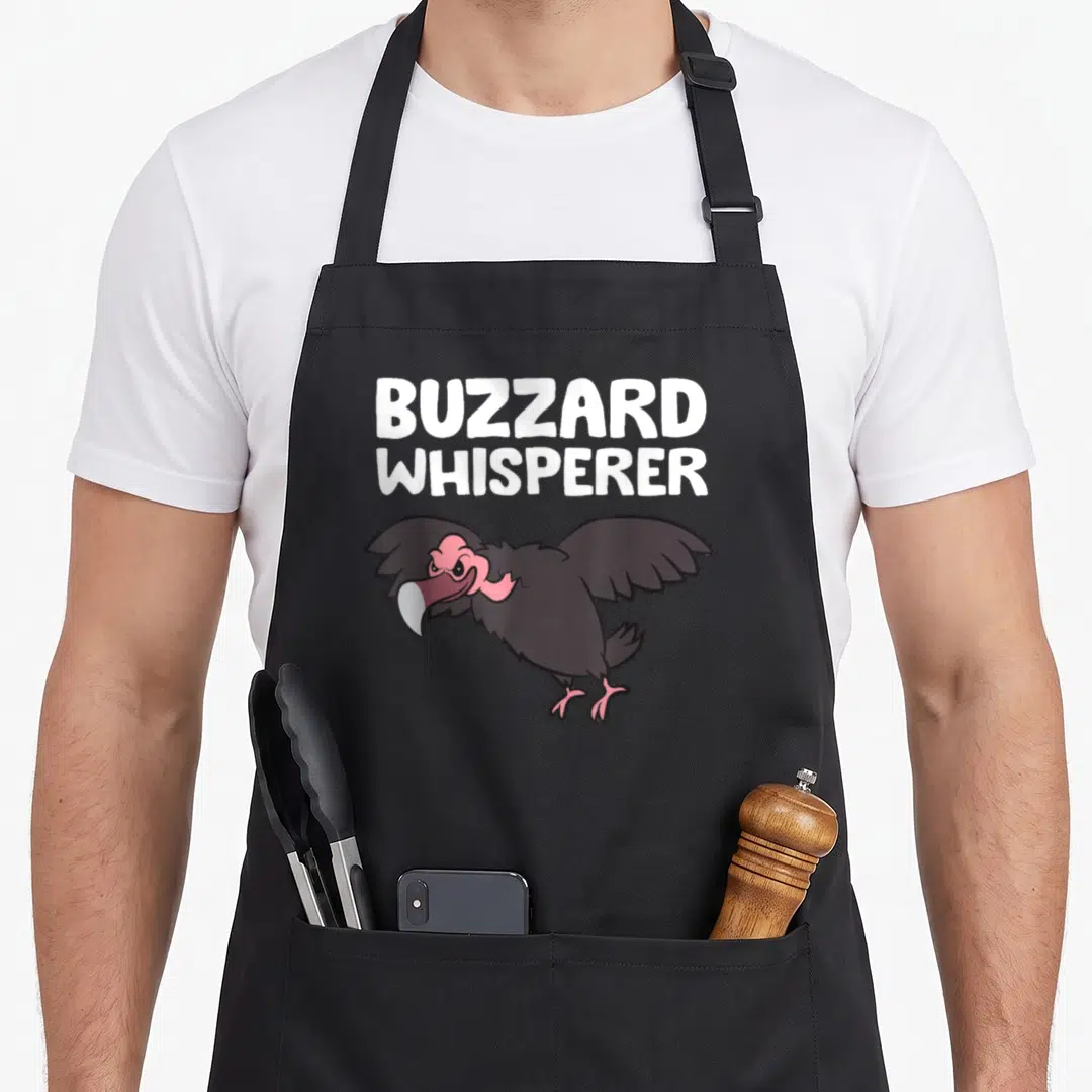 Buzzard whisperer turkey apron - Cartoon vulture with pink head and grey wings under white stacked text BUZZARD — shown on a black cotton canvas apron against a white background