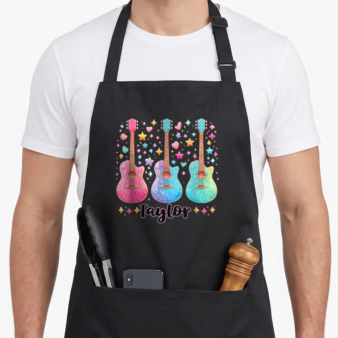 Groovy 80s apron - Three pink blue teal yellow and black guitars with scattered stars hearts and Taylor script — shown on a black cotton canvas apron against a white background