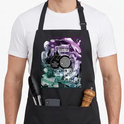 60th twilight apron - Twilight Zone 60th anniversary collage with newspaper headline and spiral logo in purple and teal — shown on a black cotton canvas apron against a white background