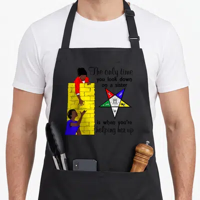 Help oes apron - Two women by yellow wall helping each other near multi-colored star with text — shown on a black cotton canvas apron against a white background