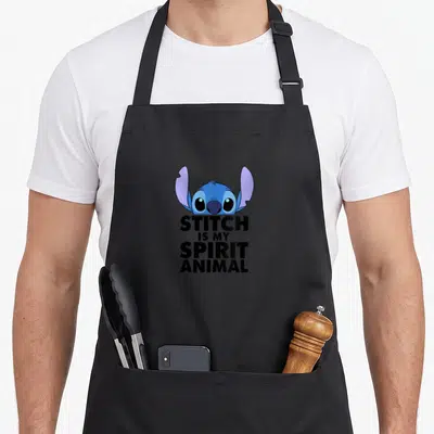 Creature apron - Blue cartoon head above black text STITCH IS MY SPIRIT ANIMAL on black fabric — shown on a black cotton canvas apron against a white background