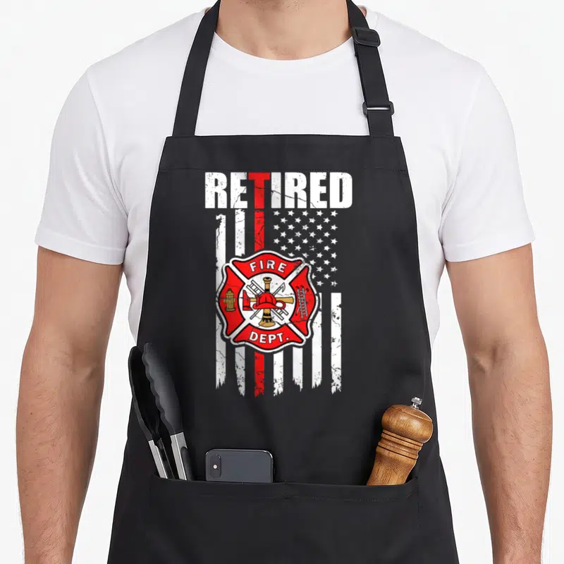 Flag firefighter cooking apron - Distressed American flag with red line and Fire Dept Maltese cross emblem — shown on a black cotton canvas apron against a white background