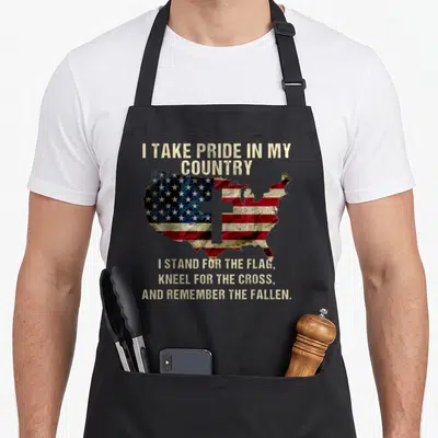Pride patriotic aprons - Distressed USA flag map with cross and text I stand for the flag kneel for the cross — shown on a black cotton canvas apron against a white background