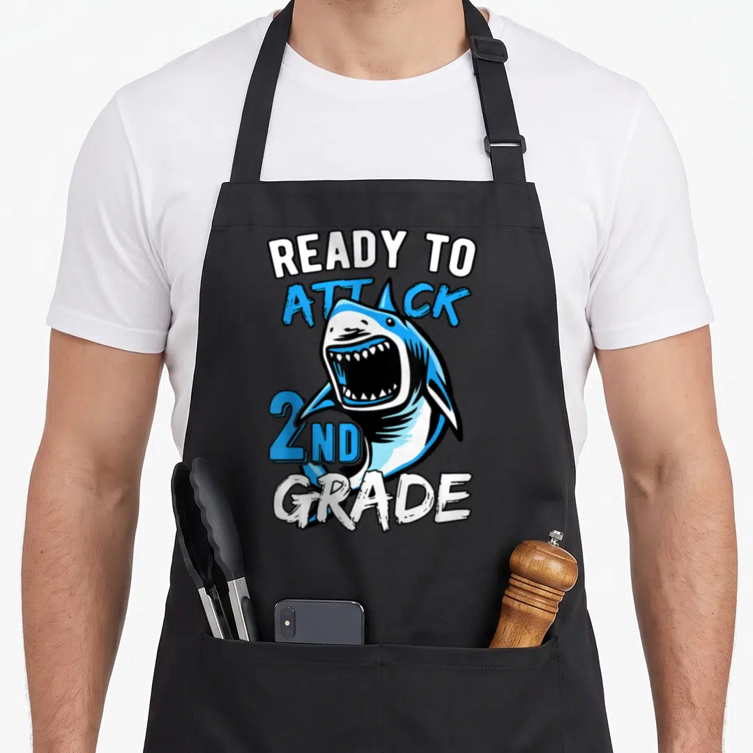 Attack 2nd apron - Cartoon shark with READY TO ATTACK 2ND GRADE text in blue white black — shown on a black cotton canvas apron against a white background