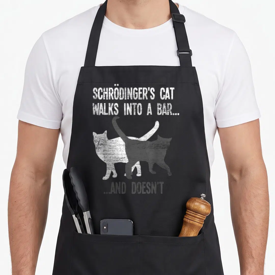 Walk cat apron - Schrödinger's Cat walks into a bar text with overlapping white and black cat silhouettes — shown on a black cotton canvas apron against a white background