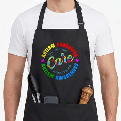 Autism caregiver apron - Central word Care filled with puzzle pieces surrounded by concentric circles of red yellow — shown on a black cotton canvas apron against a white background