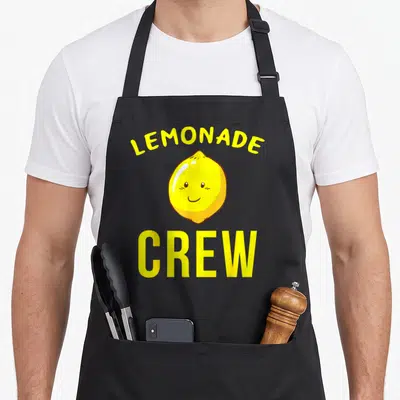 Stand crew lemonade apron - Arched LEMONADE text, smiling cartoon lemon, straight CREW text in yellow and black — shown on a black cotton canvas apron against a white background