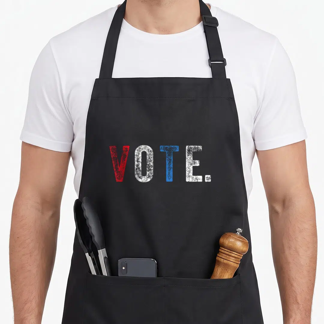 Voting novelty apron - VOTE text in red white and blue distressed font on black background — shown on a black cotton canvas apron against a white background