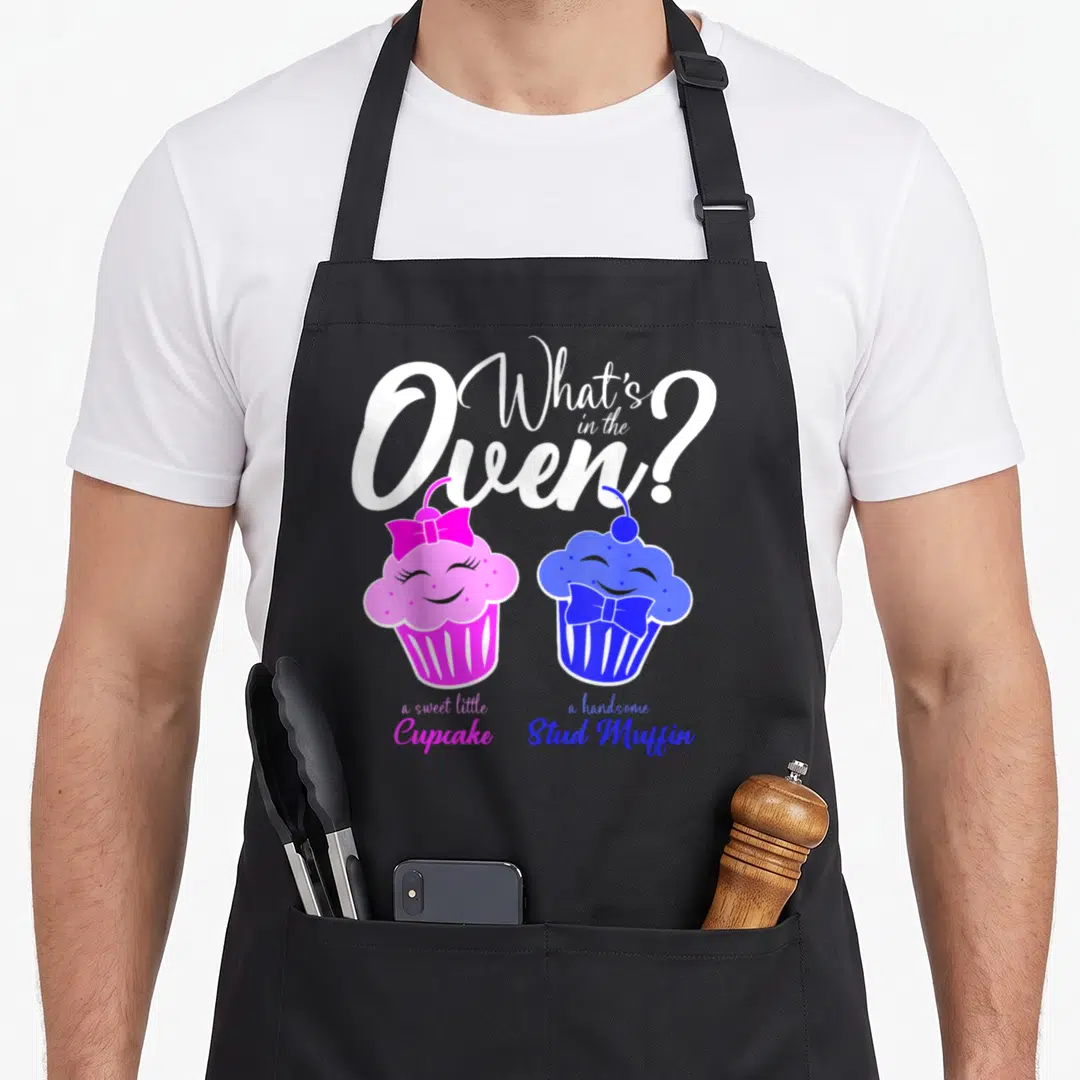 Oven muffin man apron - White script text above pink and blue anthropomorphic cupcakes with bows — shown on a black cotton canvas apron against a white background