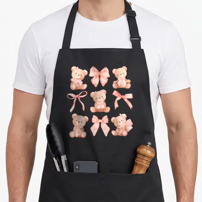 Coquette teddy bear apron - Brown teddy bears and pink bows in a watercolor 3x3 grid pattern — shown on a black cotton canvas apron against a white background