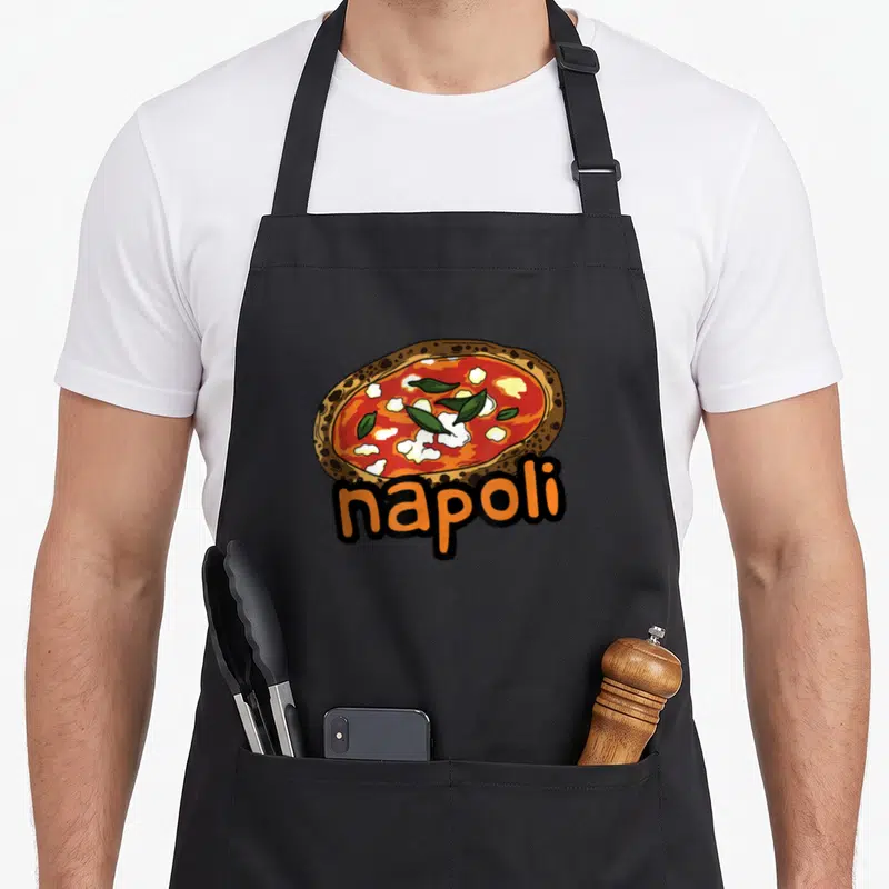 Napoli maker apron - Cartoon pizza with green leaves and orange napoli text — shown on a black cotton canvas apron against a white background