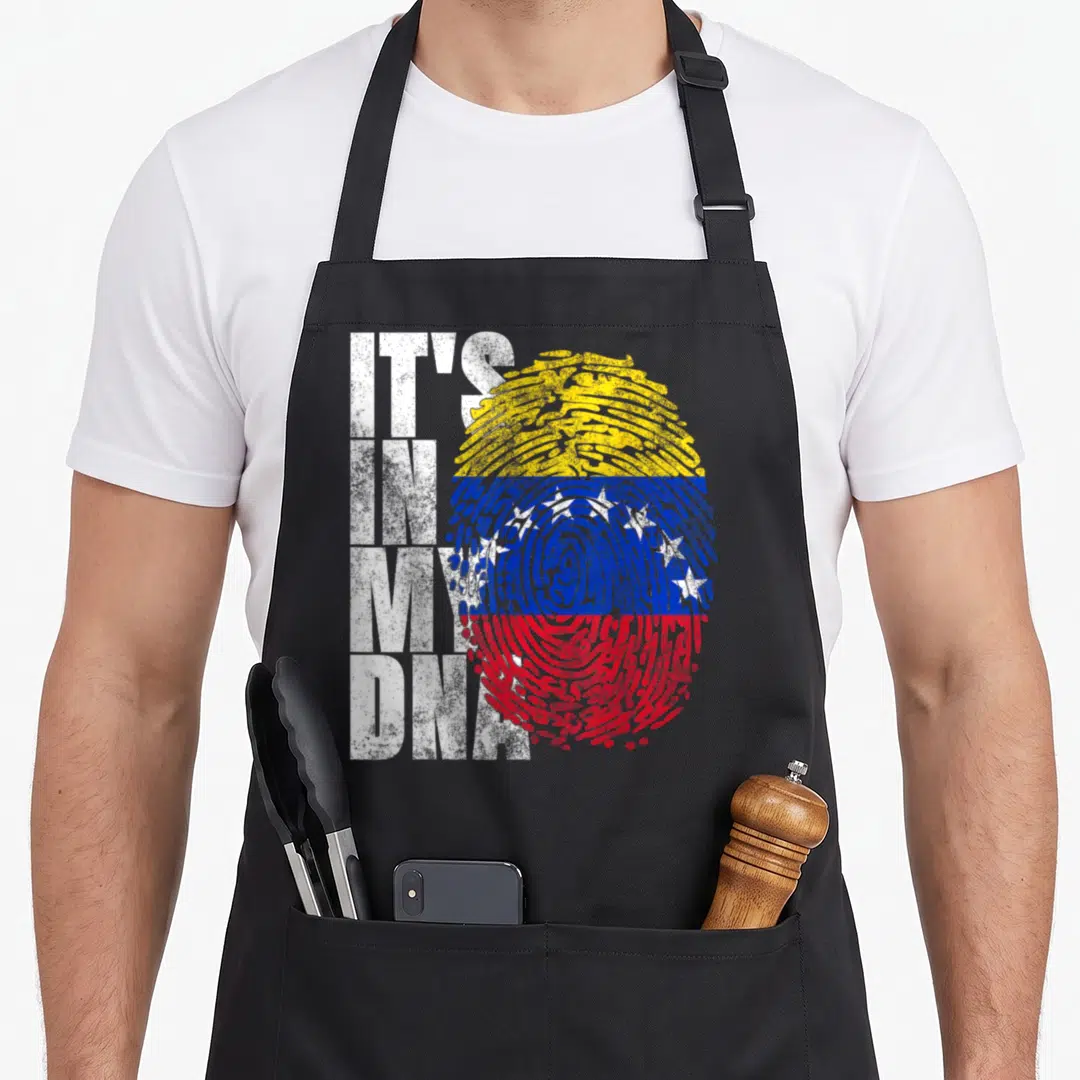 Dna venezuela apron - IT'S IN MY DNA text next to a fingerprint colored in Venezuelan flag stripes and stars — shown on a black cotton canvas apron against a white background