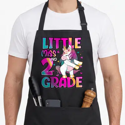 Grade unicorn 2nd apron - Dabbing unicorn with LITTLE MISS ND 2 GRADE text and hearts in pink teal yellow purple white — shown on a black cotton canvas apron against a white background