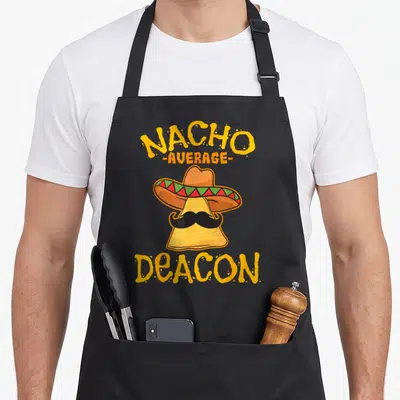 Deacon taco apron - Cartoon nacho chip with sombrero mustache and NACHO AVERAGE DEACON text — shown on a black cotton canvas apron against a white background