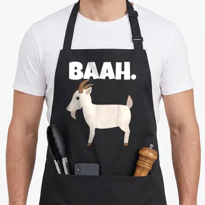Baah goat apron - Cartoon goat standing below white BAAH text — shown on a black cotton canvas apron against a white background
