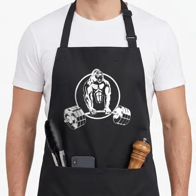 Strength gorilla mom apron - White line art of a muscular gorilla holding a barbell inside a circle on an apron — shown on a black cotton canvas apron against a white background