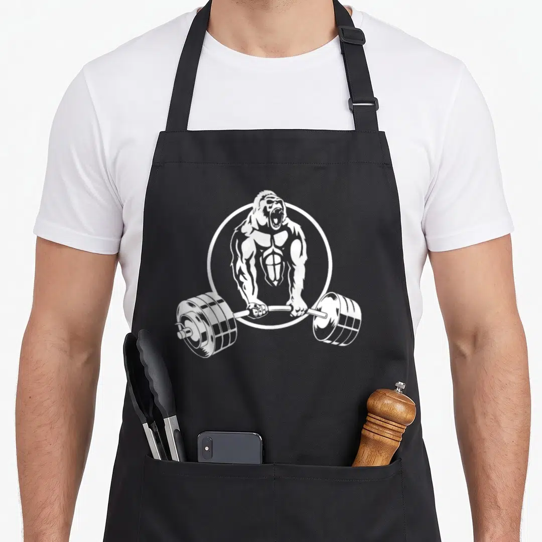 Strength gorilla mom apron - White line art of a muscular gorilla holding a barbell inside a circle on an apron — shown on a black cotton canvas apron against a white background