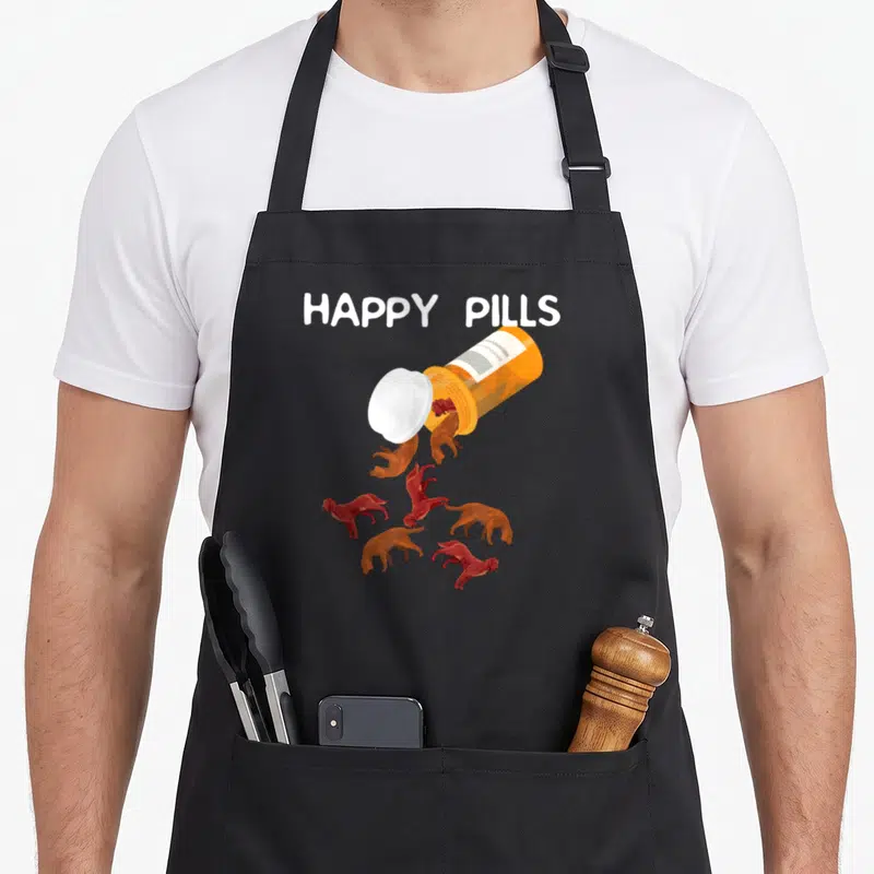 Setter irish aprons - HAPPY PILLS text above orange bottle spilling small reddish-brown dogs — shown on a black cotton canvas apron against a white background