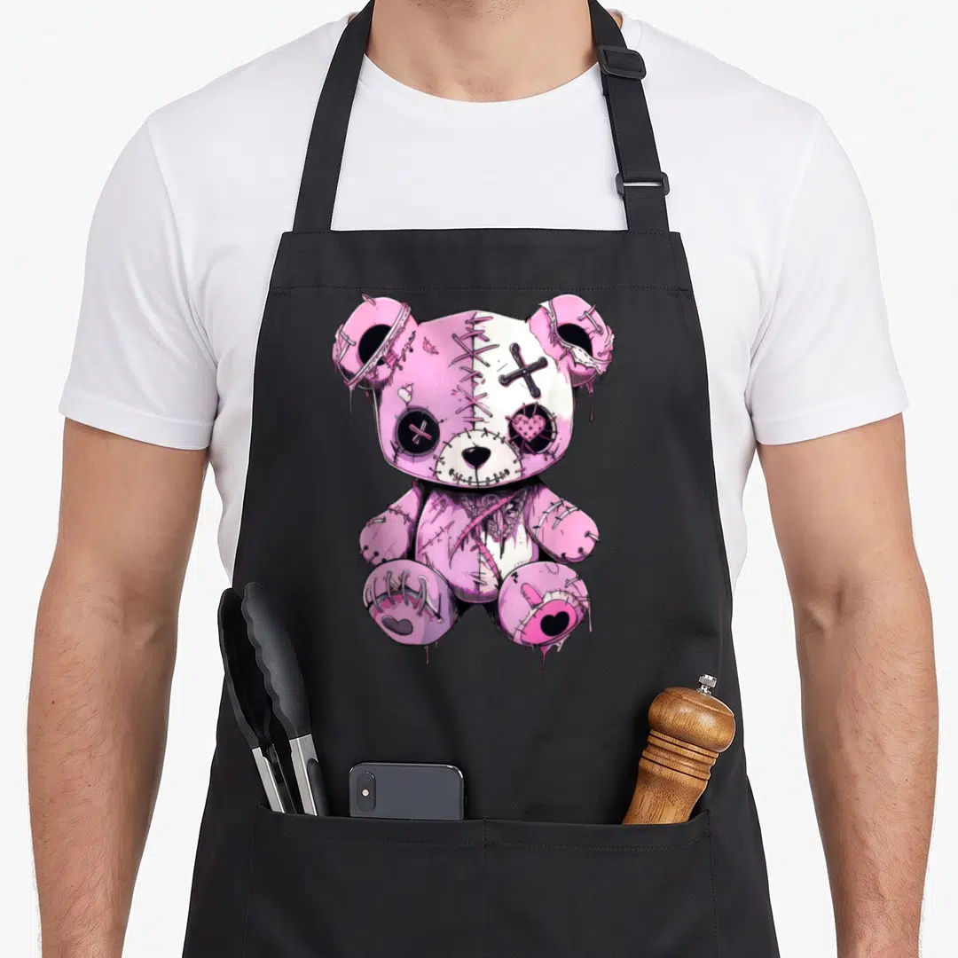 Goth kawaii anime cooking apron - Stitched pink teddy bear with black buttons and dripping paint effects in a cartoon — shown on a black cotton canvas apron against a white background