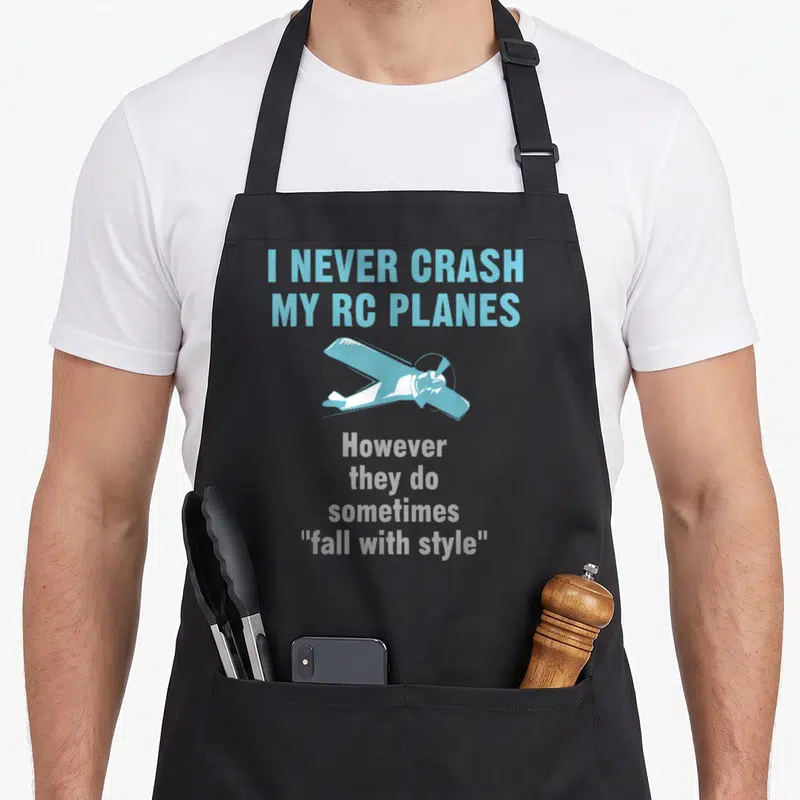 Crash hobby apron - Blue and grey RC plane illustration with text I NEVER CRASH MY RC PLANES — shown on a black cotton canvas apron against a white background