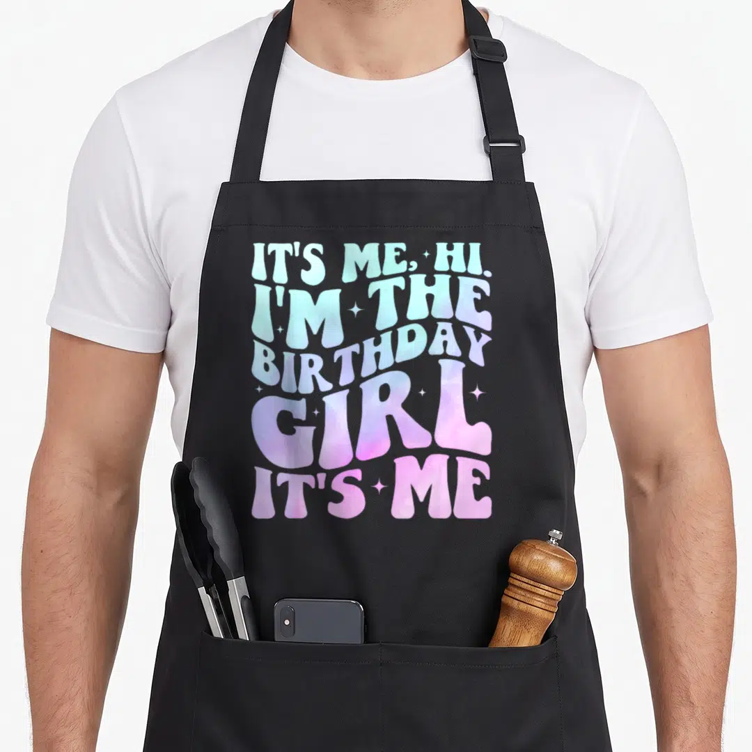 Age birthday apron for women - Gradient text reading IT'S ME HI I'M THE BIRTHDAY GIRL with small stars — shown on a black cotton canvas apron against a white background