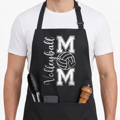 Volleyball game mother's day aprons - Vertical Volleyball text next to two M letters with a ball and heart on black — shown on a black cotton canvas apron against a white background