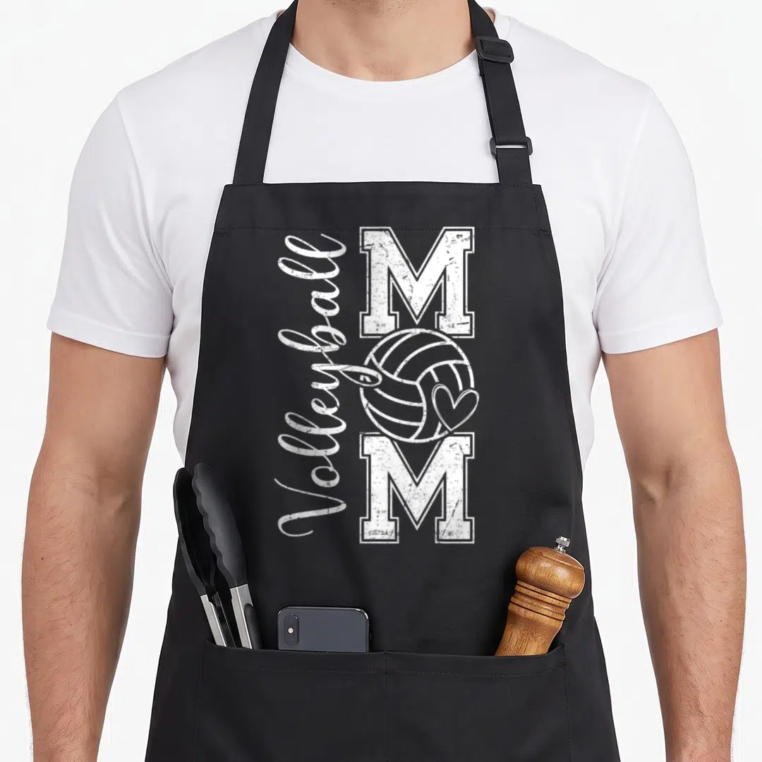 Volleyball game mother's day aprons - Vertical Volleyball text next to two M letters with a ball and heart on black — shown on a black cotton canvas apron against a white background