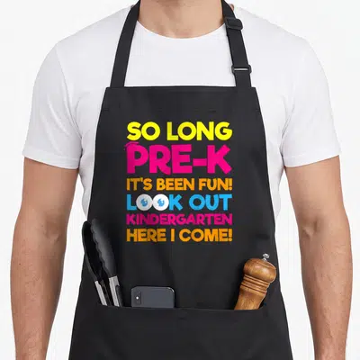 Kindergarten day pre k apron - Stacked text So Long Pre-K with graduation cap and cartoon eyes in yellow pink orange — shown on a black cotton canvas apron against a white background