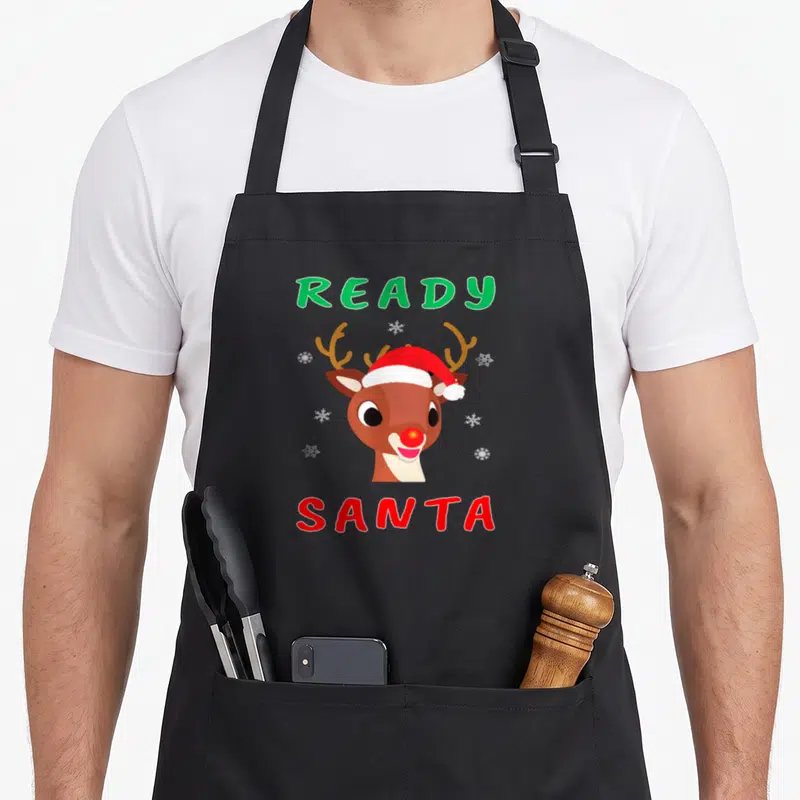 Nose red christmas apron - Cartoon reindeer head with red nose and Santa hat between green READY and red SANTA text — shown on a black cotton canvas apron against a white background