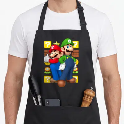 Funny thumb apron - Mario thumbs up back-to-back with Luigi surrounded by question blocks bricks coins flowers — shown on a black cotton canvas apron against a white background