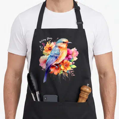 Spring the floral apron - Watercolor bird in blue and orange surrounded by pink flowers with spring fling text — shown on a black cotton canvas apron against a white background
