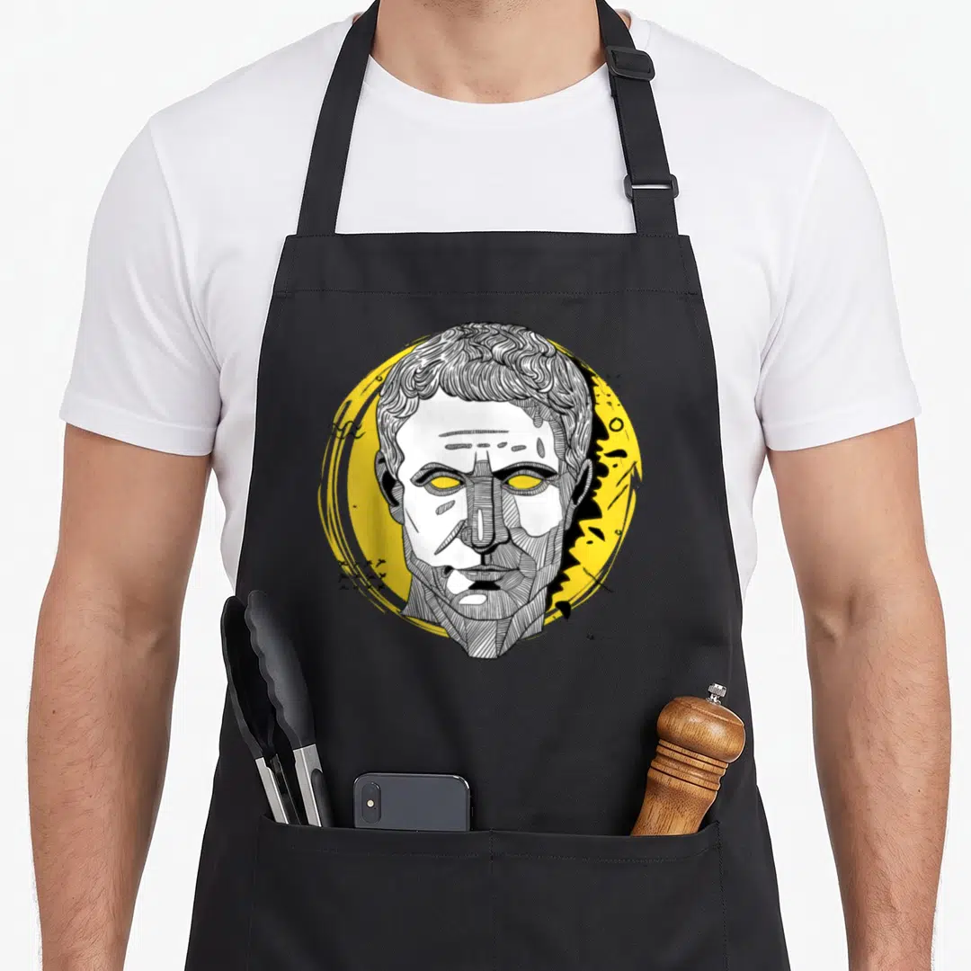 Caesar roman apron - Line art head on yellow circle with abstract black marks and white facial details — shown on a black cotton canvas apron against a white background
