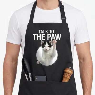 Talking cat apron - TALK TO THE PAW text above black and white cat raising paw in white circle — shown on a black cotton canvas apron against a white background