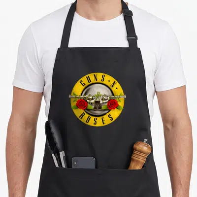 Gun bullet rose apron - Yellow circle logo with two silver revolvers, red roses, and GUNS N ROSES text — shown on a black cotton canvas apron against a white background