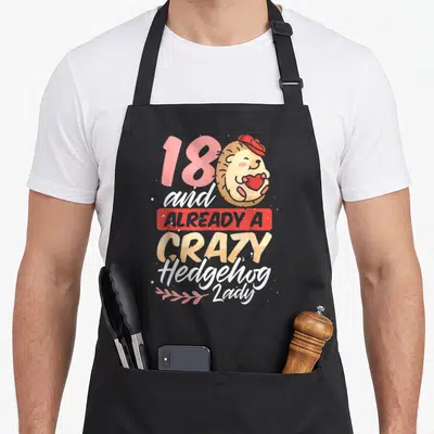 Already crazy hedgehog lady apron - Cartoon hedgehog holding red heart next to number 18 and stacked text — shown on a black cotton canvas apron against a white background