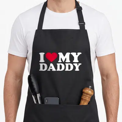 Cute daddy apron - I MY DADDY text with red heart symbol in white lettering — shown on a black cotton canvas apron against a white background