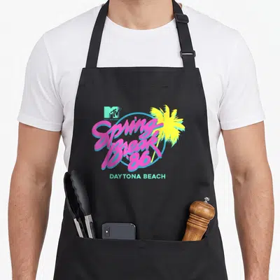 Vintage mtv spring aprons - Pink script reading Spring Break '86 over blue circle and yellow palm tree with Daytona — shown on a black cotton canvas apron against a white background