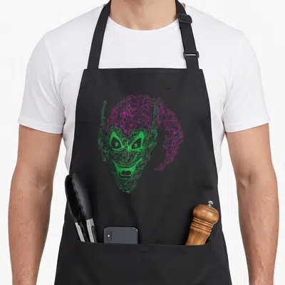Norman goblin apron - Green and pink line art face formed by clusters of smaller heads — shown on a black cotton canvas apron against a white background