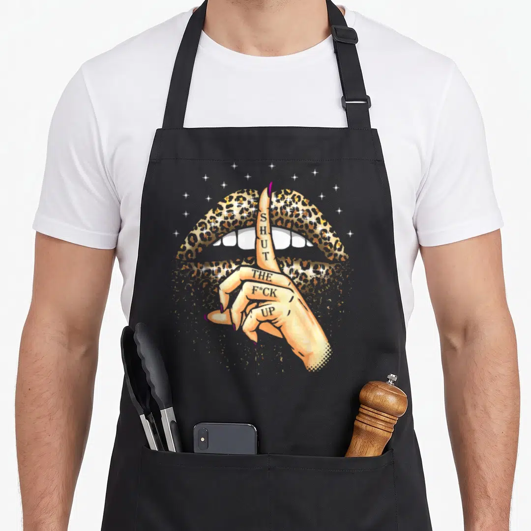 Gag leopard apron - Cartoon hand with tattoo text over leopard lips and stars — shown on a black cotton canvas apron against a white background