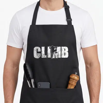 Climbing bouldering addict apron - White distressed CLIMB text with climber silhouette replacing the letter I — shown on a black cotton canvas apron against a white background